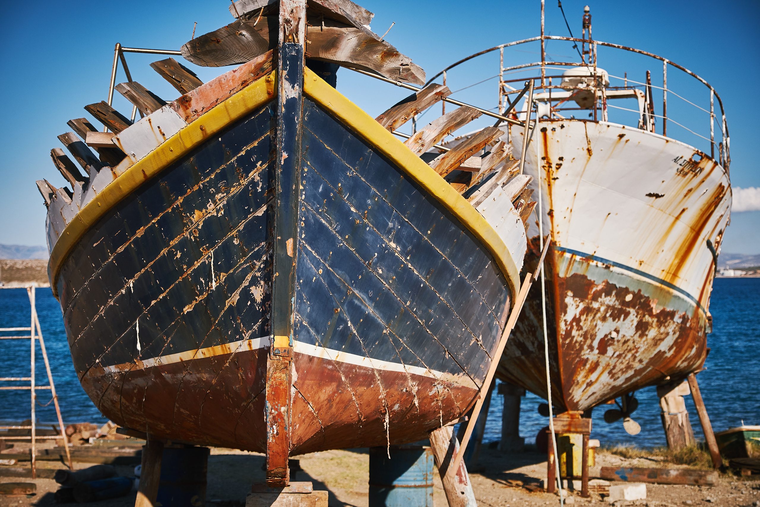 Beautiful view of two rusted boats on the beach with the blue sea in the background